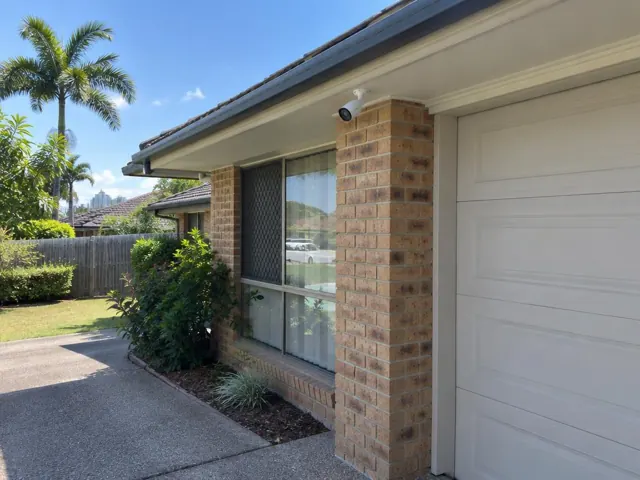 White CCTV camera mounted under the eave on a brick house exterior in Bundall