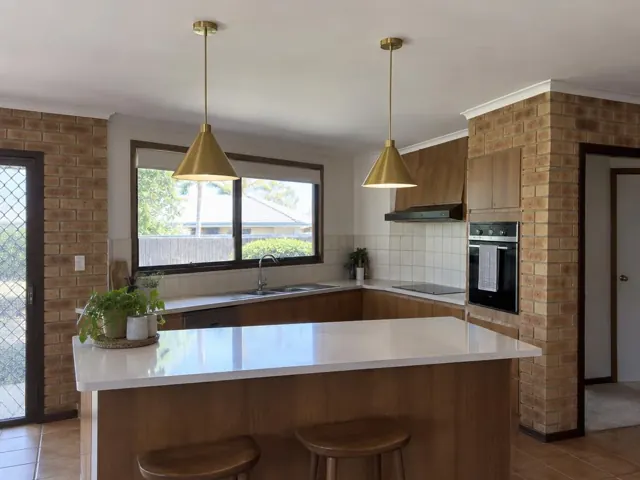 Two brass pendant lights over a kitchen island in a brick and timber home in Carrara